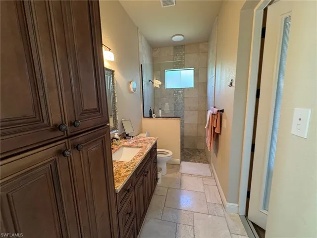 Bathroom featuring toilet, vanity, and tiled shower
