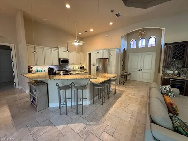 Kitchen featuring decorative backsplash, appliances with stainless steel finishes, decorative light fixtures, and a high ceiling