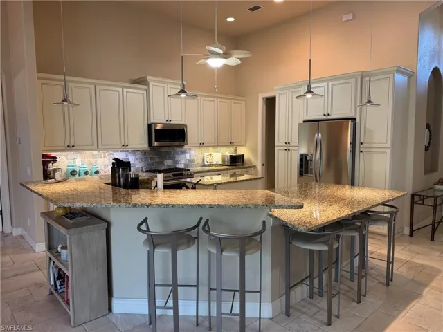 Kitchen with pendant lighting, a high ceiling, a kitchen bar, kitchen peninsula, and stainless steel appliances