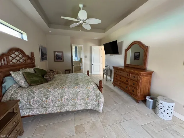 Bedroom featuring ensuite bath, a raised ceiling, and ceiling fan