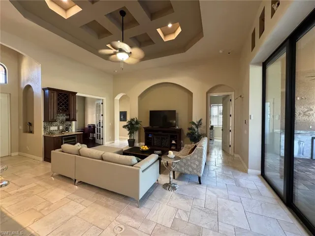 Living room with bar area, ceiling fan, a towering ceiling, and coffered ceiling