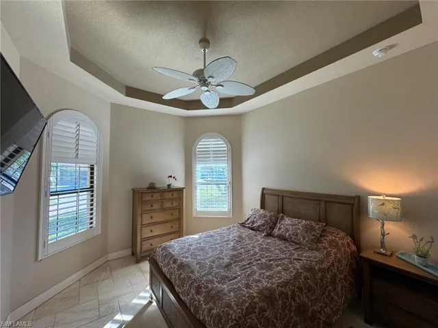 Tiled bedroom featuring a tray ceiling, multiple windows, ceiling fan, and a textured ceiling