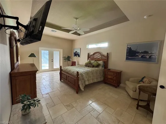Bedroom with french doors, ceiling fan, a raised ceiling, and multiple windows