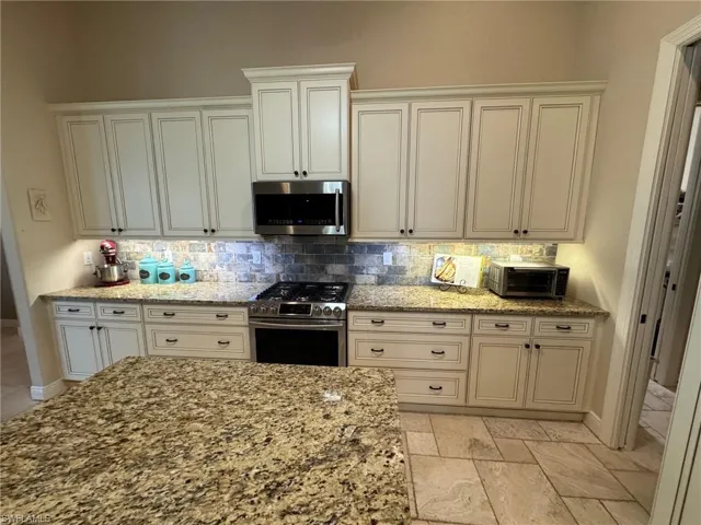 Kitchen with light stone counters, white cabinetry, backsplash, and appliances with stainless steel finishes