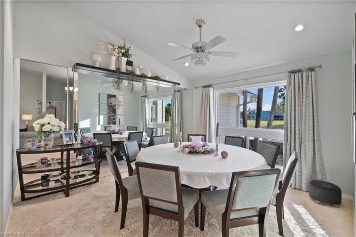 Dining area featuring vaulted ceiling, light colored carpet, ceiling fan, and plenty of natural light