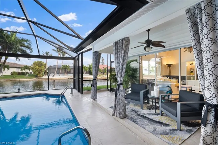 View of swimming pool featuring a patio, ceiling fan, glass enclosure, and a water view