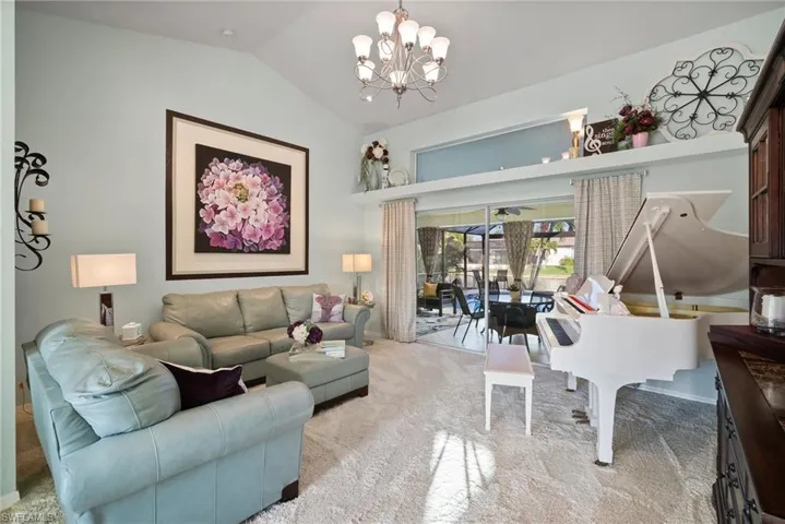 Living room featuring vaulted ceiling, light colored carpet, and a notable chandelier
