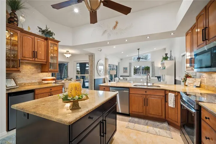 Kitchen featuring light stone counters, kitchen peninsula, sink, backsplash, and appliances with stainless steel finishes