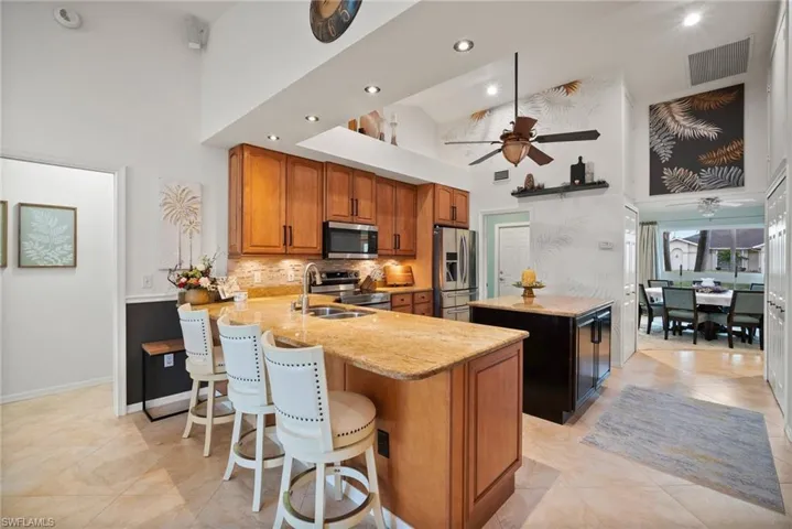 Kitchen with kitchen peninsula, appliances with stainless steel finishes, light stone countertops, high vaulted ceiling, and a center island
