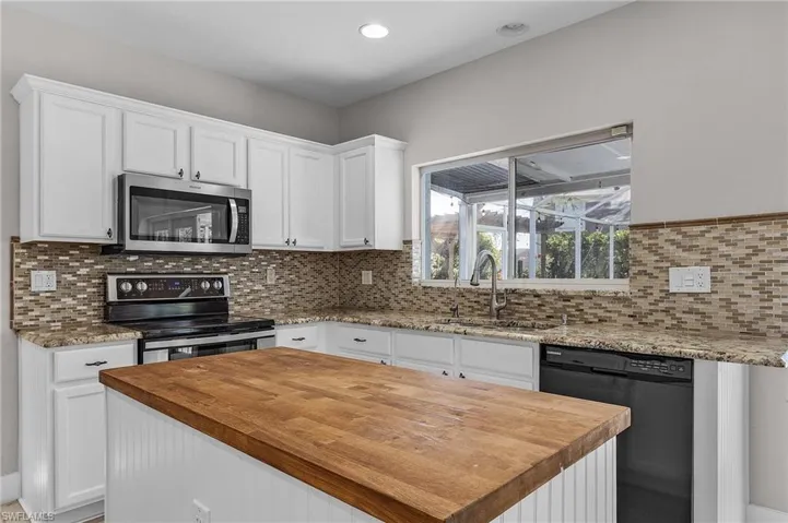 Kitchen featuring backsplash, sink, appliances with stainless steel finishes, a kitchen island, and white cabinetry