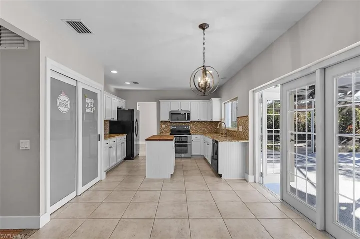 Kitchen featuring wood counters, an inviting chandelier, black appliances, white cabinets, and decorative light fixtures