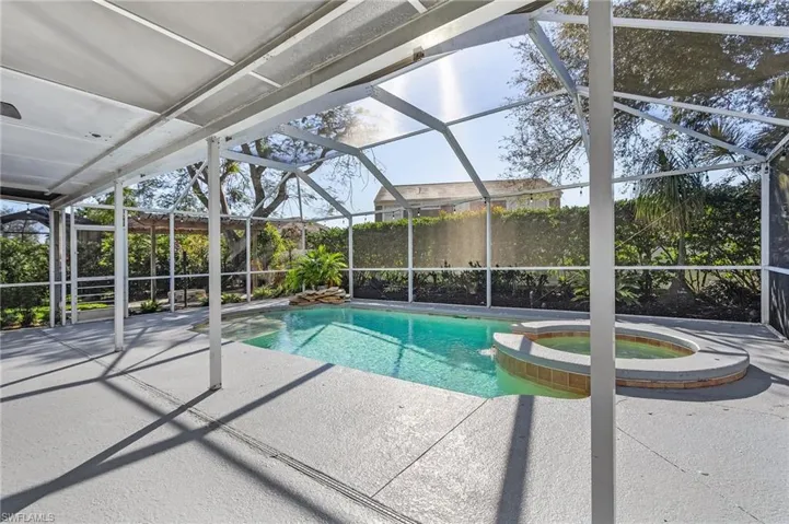 View of swimming pool featuring glass enclosure, a patio area, and an in ground hot tub