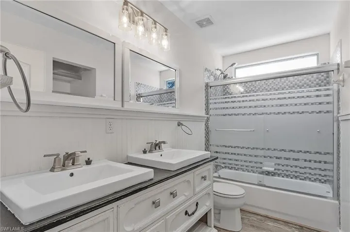 Full bathroom featuring combined bath / shower with glass door, wood-type flooring, vanity, and toilet