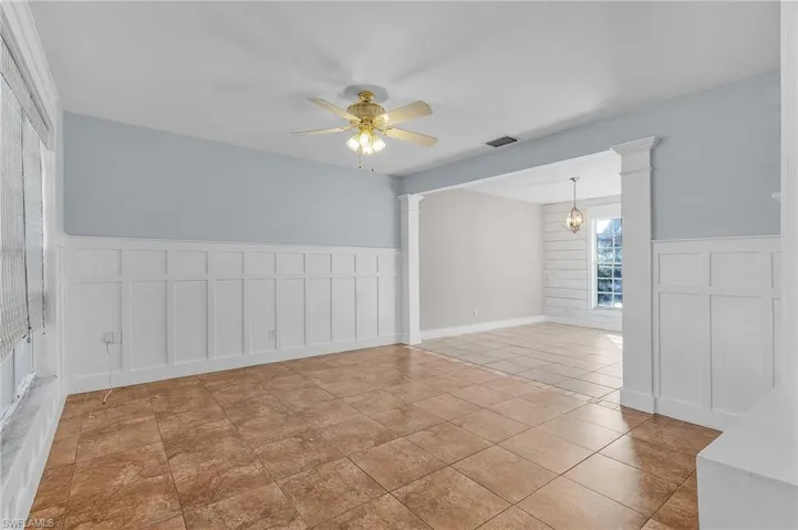 Empty room with ornate columns, light tile patterned floors, and ceiling fan with notable chandelier