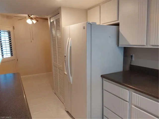 Kitchen featuring white refrigerator with ice dispenser, light tile patterned flooring, white cabinets, and a ceiling fan