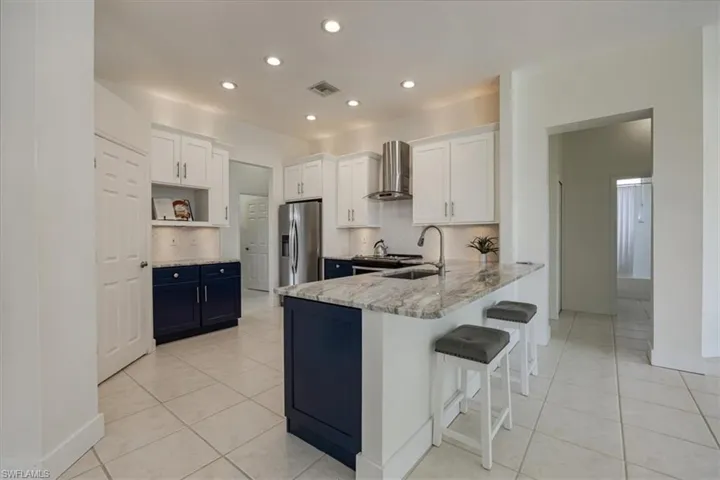 Upgraded kitchen with blue cabinets and stainless steel appliances and bar with door to hallway