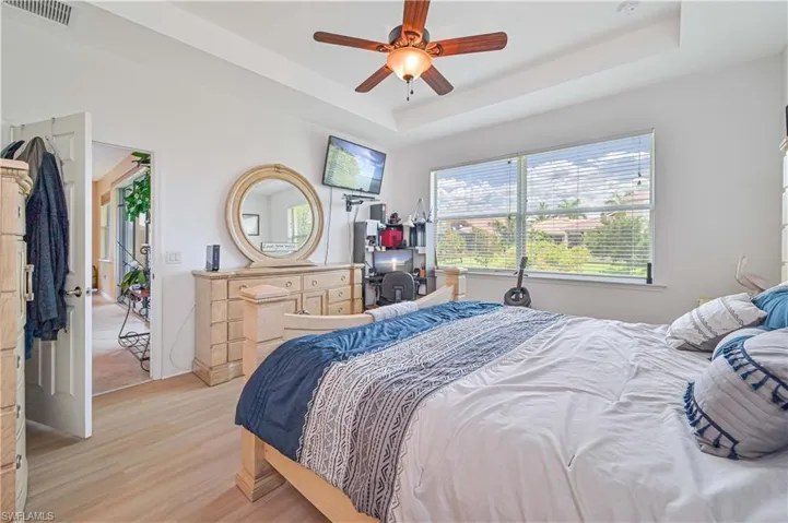 Bedroom with a raised ceiling, ceiling fan, and light hardwood / wood-style flooring