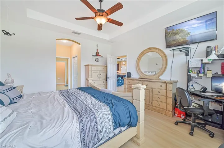 Bedroom with ceiling fan, a tray ceiling, and light hardwood / wood-style flooring