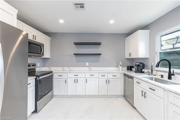 Kitchen with stainless steel appliances, white cabinetry, open shelves, light stone counters, and recessed lighting