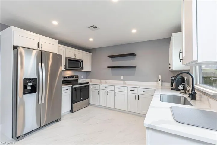 Kitchen with open shelves, appliances with stainless steel finishes, white cabinets, light stone counters, and recessed lighting