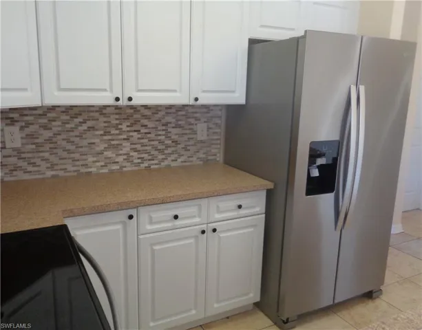 Kitchen featuring white cabinets, backsplash, stainless steel side by side door refrigerator with ice dispenser, backsplash, light tile patterned floors, and light countertops