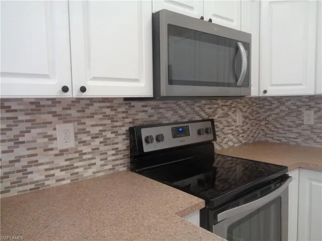 Kitchen with stainless steel microwave, stove & oven, backsplash, white cabinetry, and light countertops