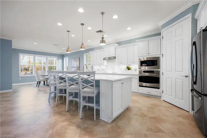 Kitchen featuring decorative light fixtures, a center island with sink, white cabinets, appliances with stainless steel finishes, and recessed lighting