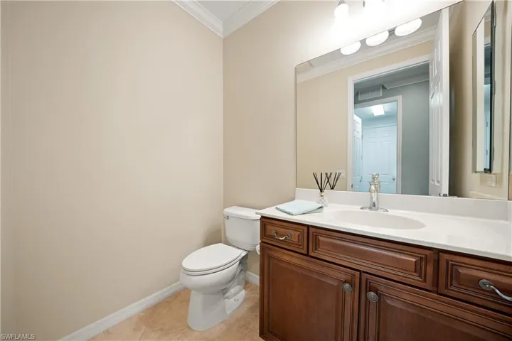 Half bathroom with vanity, ornamental molding, and light tile patterned flooring