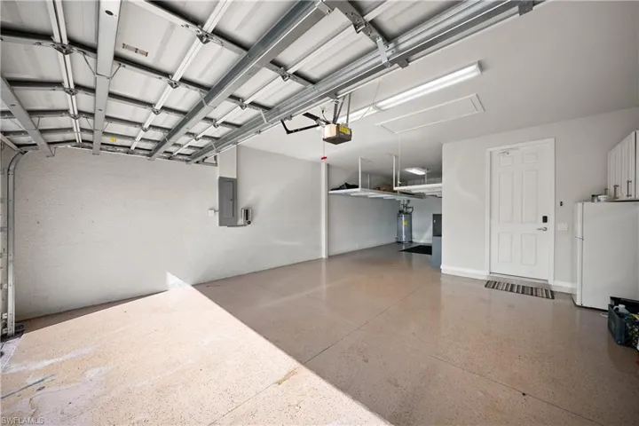 Garage with freestanding refrigerator, electric panel, water heater, and a garage door opener