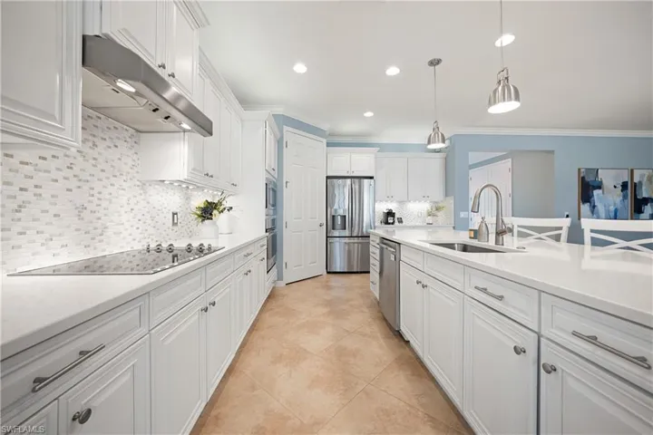 Kitchen featuring white cabinets, stainless steel appliances, decorative light fixtures, under cabinet range hood, and light stone countertops