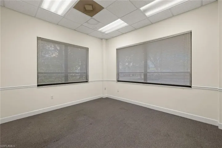 Empty room featuring dark carpet and a paneled ceiling