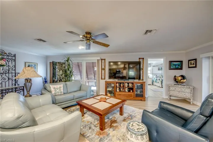 Large Great room looking back to the entry foyer and large impact rated windows. The spacious master suite is to the right. Features include LVP flooring, crown molding, impact rated sliding glass doors that pocket into the wall and lead to a beautiful view of the Lanai and Pool area.