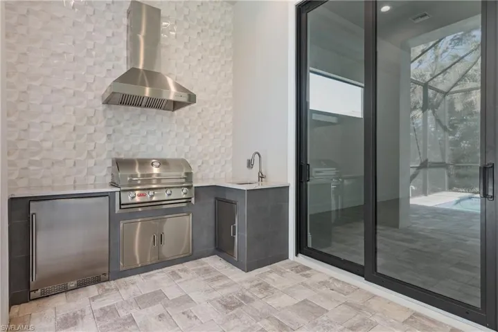 View of patio / terrace featuring grilling area, sink, glass enclosure, and an outdoor kitchen