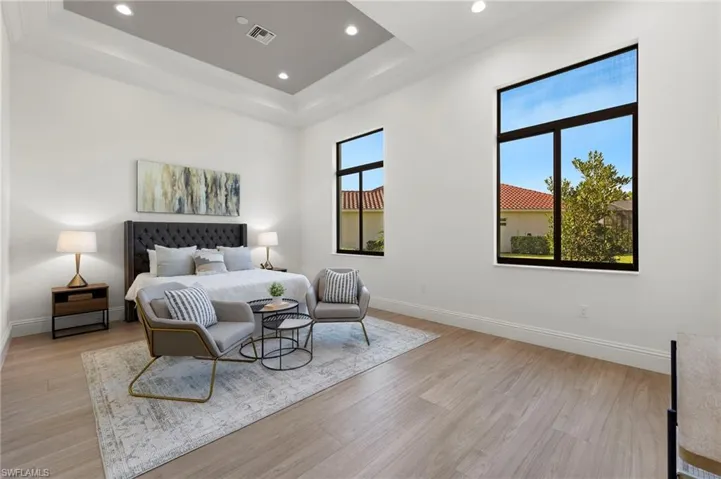 Bedroom featuring a raised ceiling, multiple windows, and light wood-type flooring