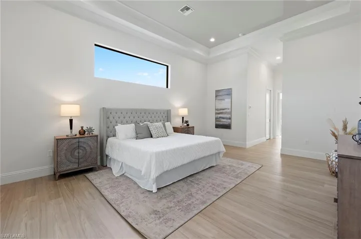 Bedroom with light hardwood / wood-style floors, crown molding, and a towering ceiling