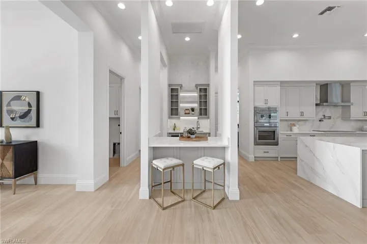 Kitchen with light hardwood / wood-style floors, tasteful backsplash, wall chimney exhaust hood, and double oven