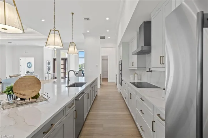 Kitchen featuring wall chimney range hood, sink, pendant lighting, appliances with stainless steel finishes, and light stone counters