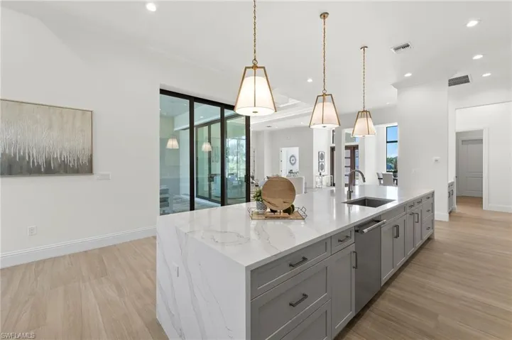 Kitchen featuring sink, stainless steel dishwasher, gray cabinets, light stone counters, and a kitchen island with sink
