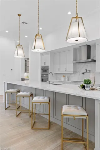 Kitchen featuring light stone countertops, wall chimney range hood, and light hardwood / wood-style flooring