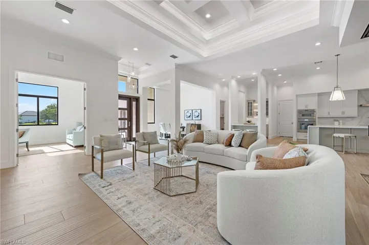 Living room with a towering ceiling, light hardwood / wood-style floors, coffered ceiling, beamed ceiling, and crown molding