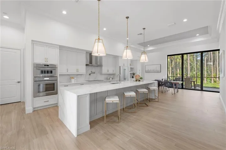 Kitchen with a spacious island, stainless steel double oven, light hardwood / wood-style flooring, decorative light fixtures, and light stone counters