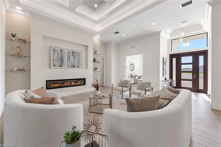 Living room with light hardwood / wood-style floors, crown molding, a towering ceiling, and beam ceiling