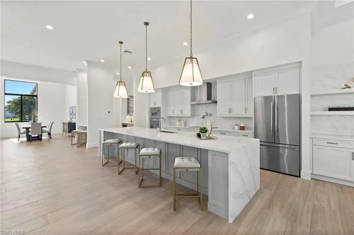Kitchen with a spacious island, decorative light fixtures, appliances with stainless steel finishes, light stone counters, and tasteful backsplash