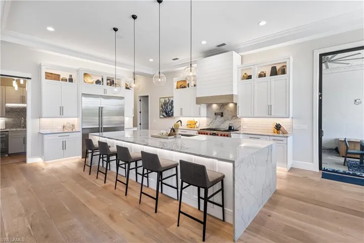 Contemporary waterfall-edge quartz island measuring 14 ft. x 6.5ft. Custom wood cabinetry. Recess lighting throughout. WOLFE 6 burner stove w/hood and pot filler. Sub Zero Fridge/Freezer, Bosch dishwasher and WOLFE microwave. Canal and pool views.
