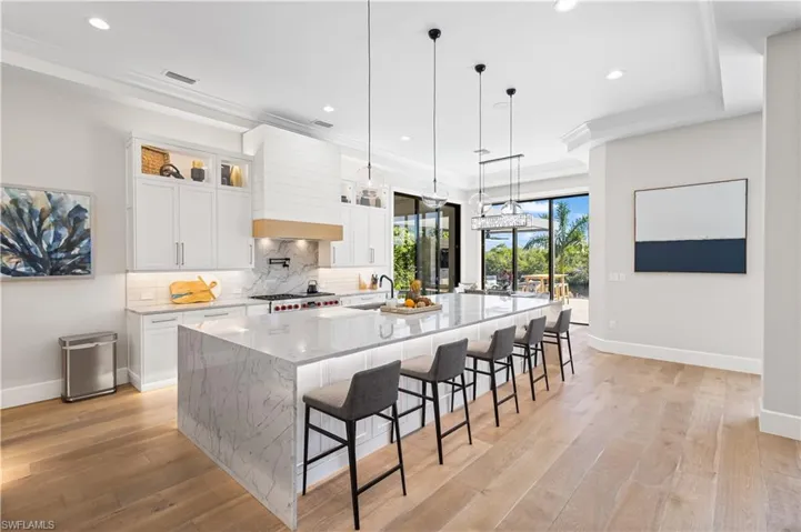 Contemporary waterfall-edge quartz island measuring 14 ft. x 6.5ft. Custom wood cabinetry. Recess lighting throughout. WOLFE 6 burner stove w/hood and pot filler. Sub Zero Fridge/Freezer, Bosch dishwasher and WOLFE microwave. Canal and pool views.