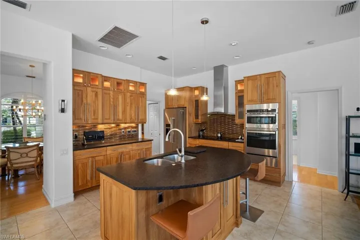Kitchen featuring hanging light fixtures, an island with sink, a healthy amount of sunlight, and wall chimney range hood