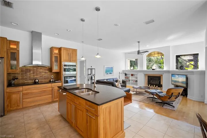 Kitchen featuring stainless steel appliances, a kitchen island with sink, sink, wall chimney range hood, and hanging light fixtures