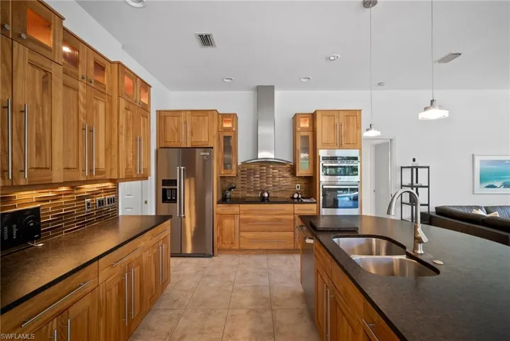 Kitchen with decorative backsplash, wall chimney exhaust hood, stainless steel appliances, sink, and hanging light fixtures