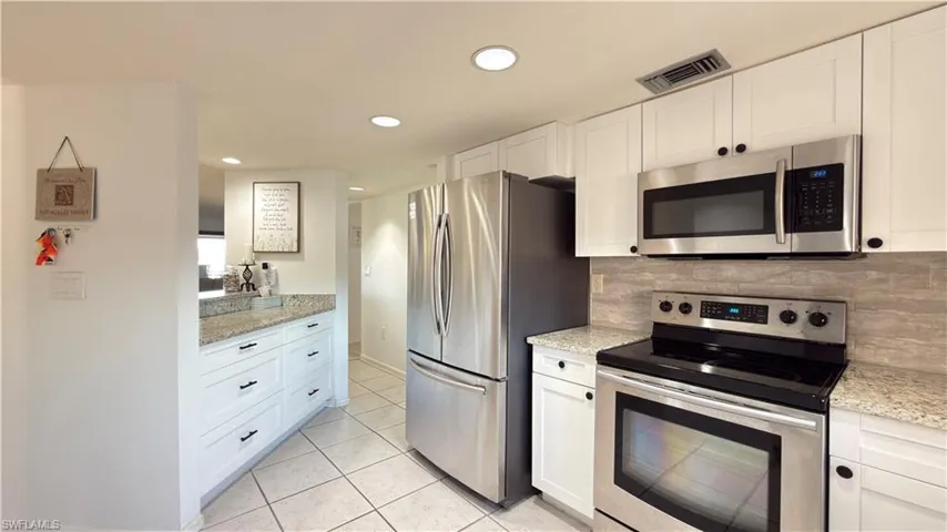 Kitchen with stainless steel appliances, white cabinets, light stone counters, recessed lighting, and light tile patterned floors