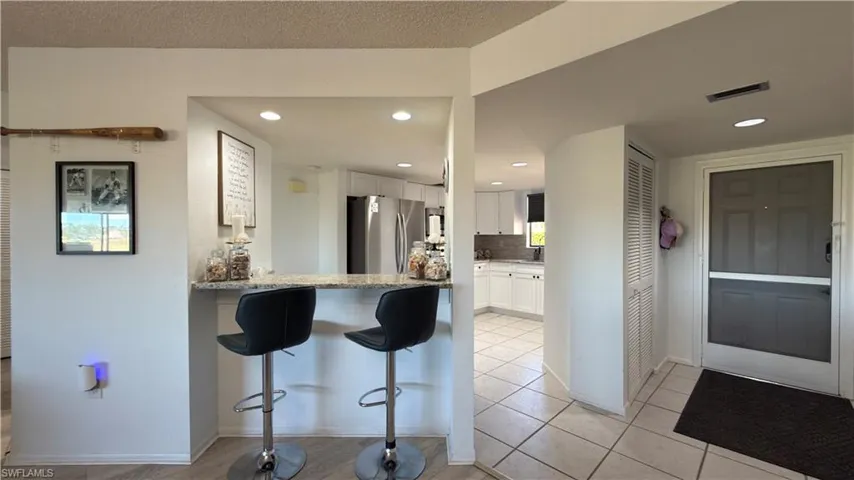 Kitchen with a breakfast bar area, white cabinets, freestanding refrigerator, light stone countertops, and backsplash